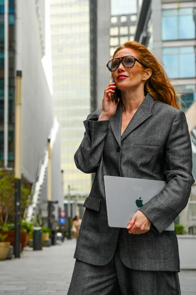 Een vrouw die in een wijk loopt met een telefoon en een computer in haar hand.